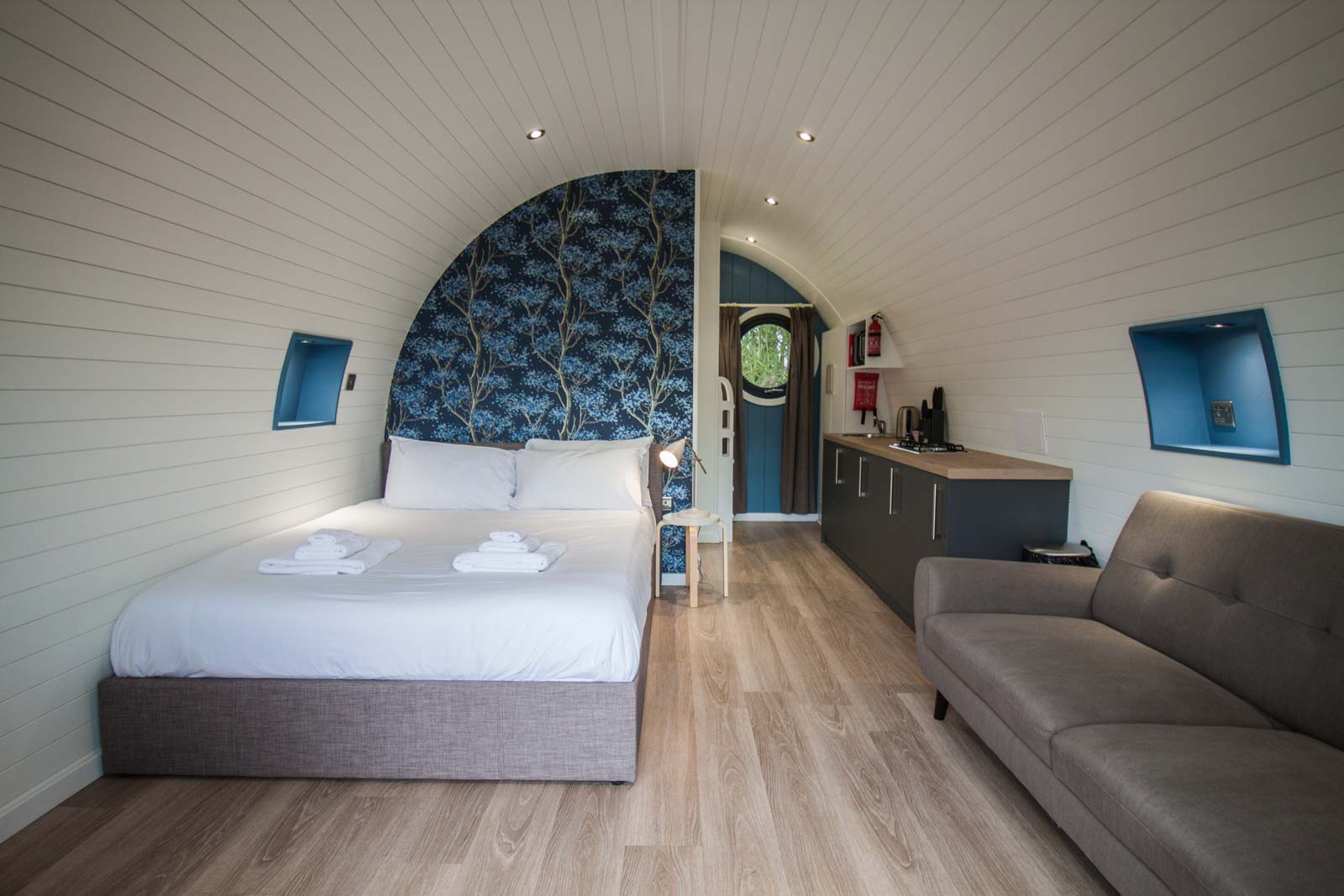 Interior of a boutique glamping pod at High Oaks Grange with sofa, Smart TV, double bed, and countryside views through circular glass doors.